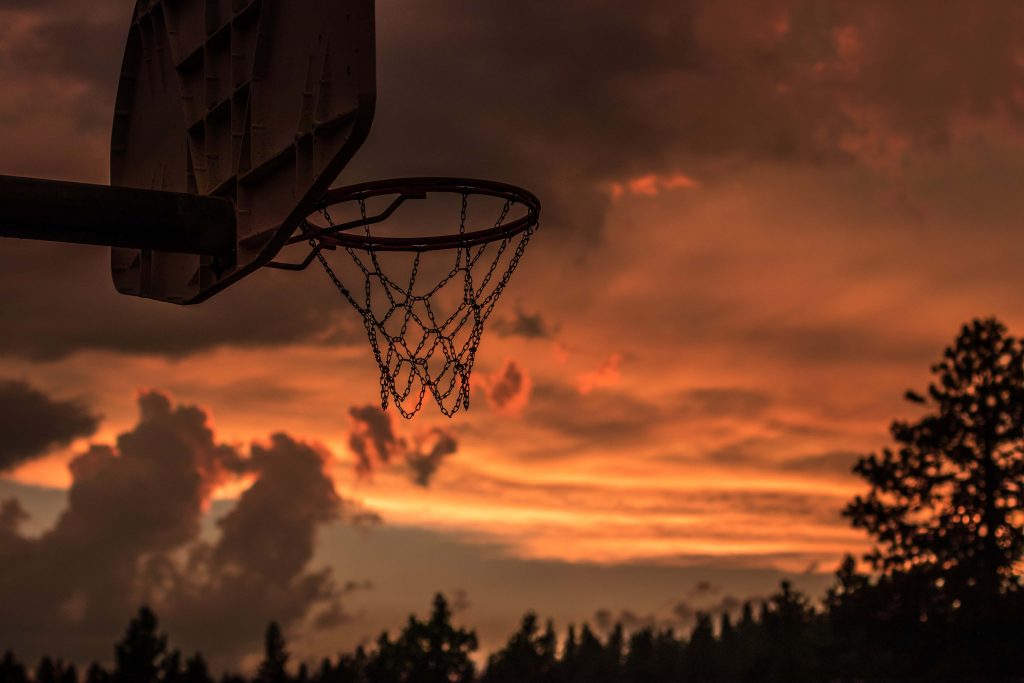Silhouette of basketball hoop with chain net at sunset vibrant orange sky sports wallpaper background