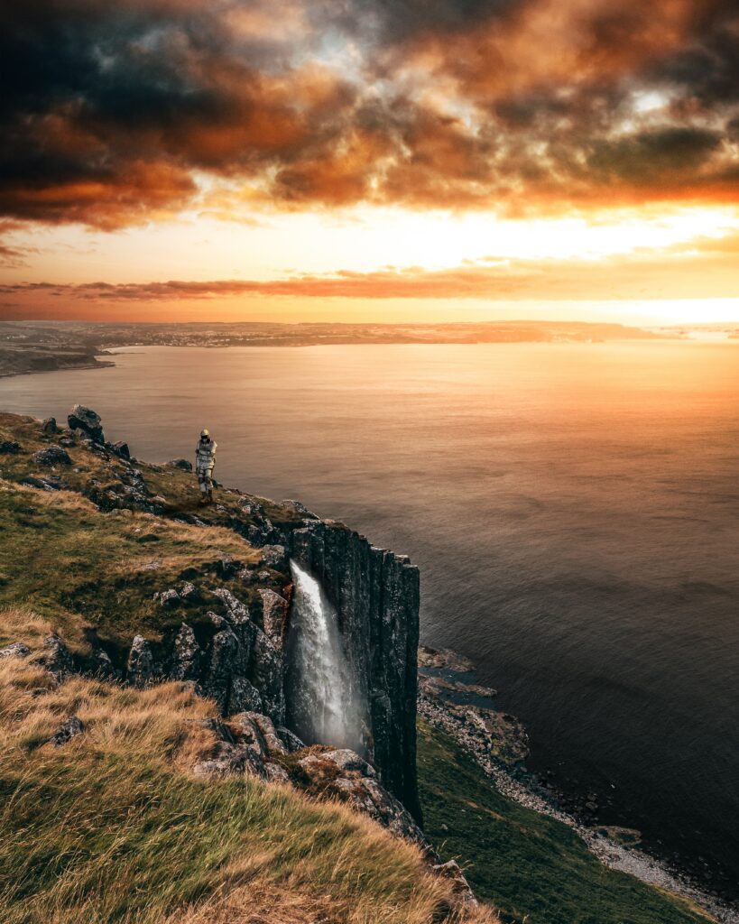 Dramatic cliffs waterfall and sea at sunset with golden orange and deep blue sky wallpaper background