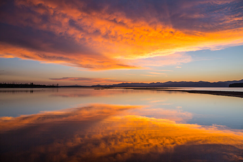 Fiery sunset horizon with vibrant orange purple clouds reflecting on calm water surface wallpaper