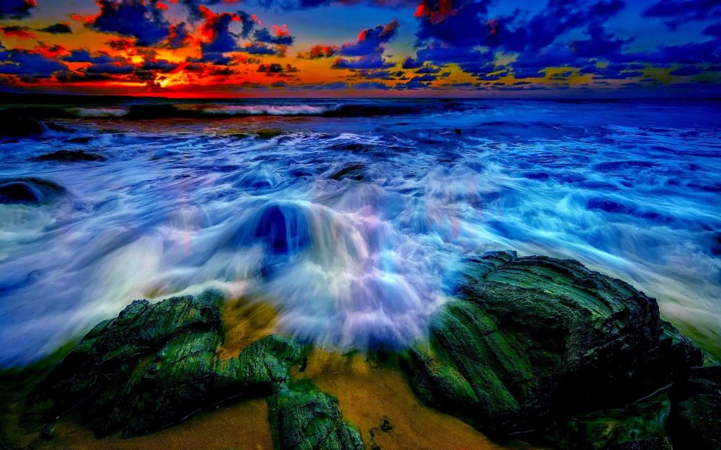 Vibrant sunset ocean waves crashing on dark rugged rocks 4K Ultra HD serene wallpaper background