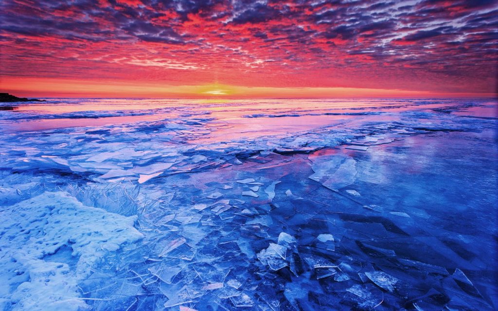 Frozen lake with shattered ice shards at sunset vibrant red orange sky serene winter landscape Wallpaper