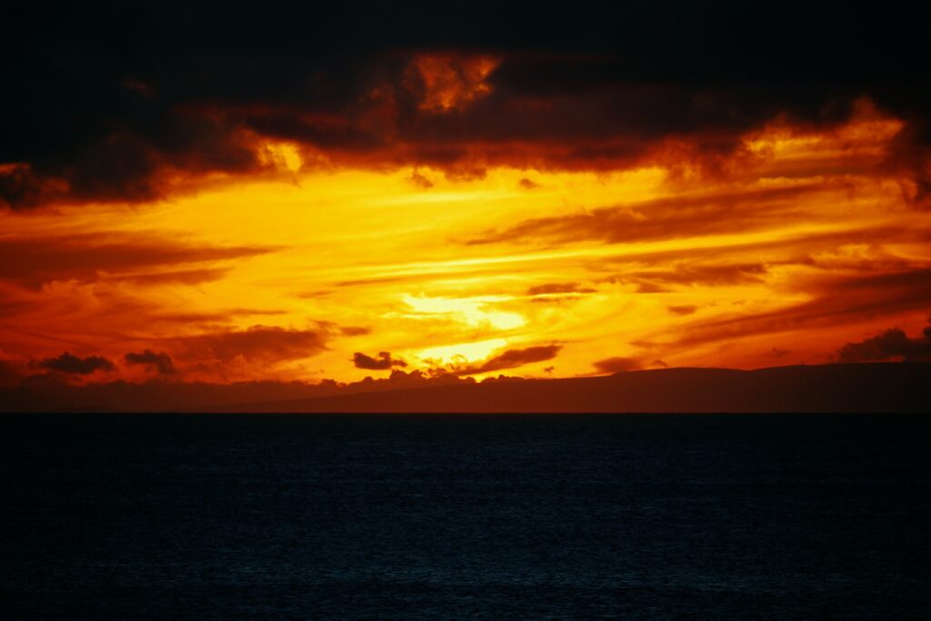 Fiery sunset wallpaper over sea with orange yellow sky dark clouds and deep blue water background
