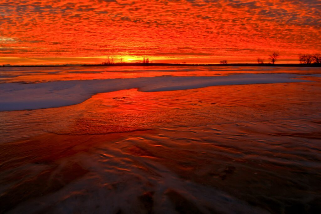 Sunset over snowy shore with vibrant orange and red sky reflecting on icy landscape wallpaper
