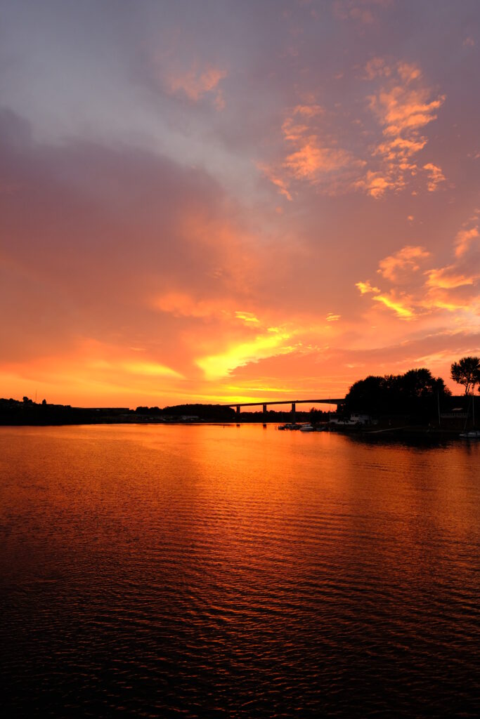 Fiery sunset river scene with orange sky and gentle ripples creating serene wallpaper background