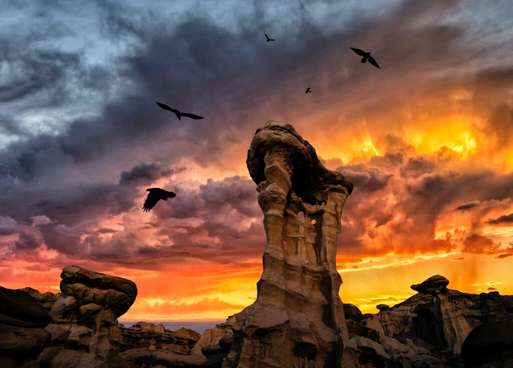 Dramatic rock formations at sunset with swirling clouds and soaring birds vibrant landscape wallpaper