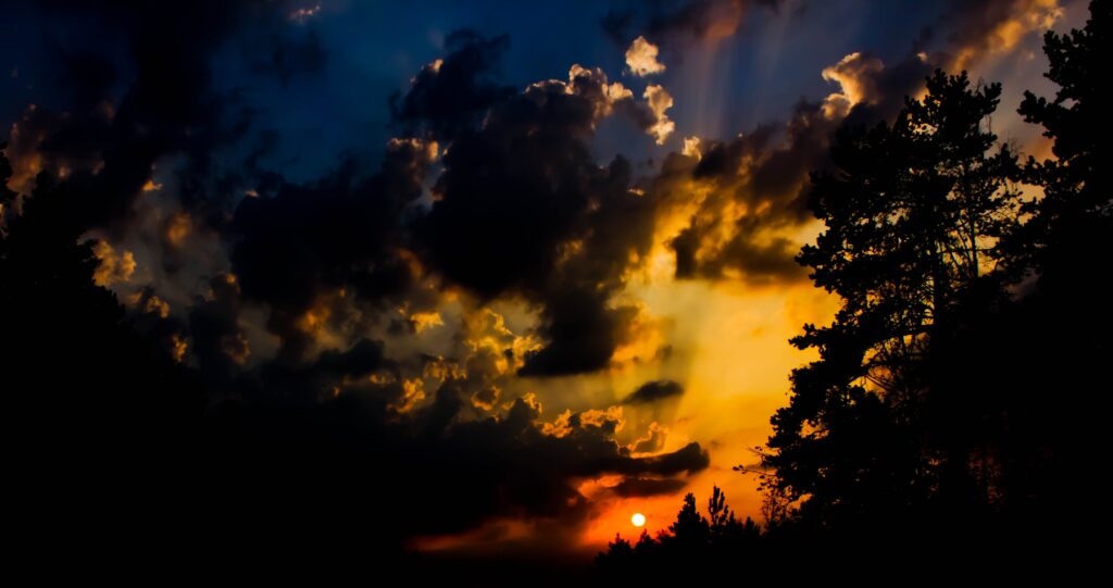 Dramatic sunset wallpaper with fiery orange sky dark clouds silhouetted trees moody atmosphere