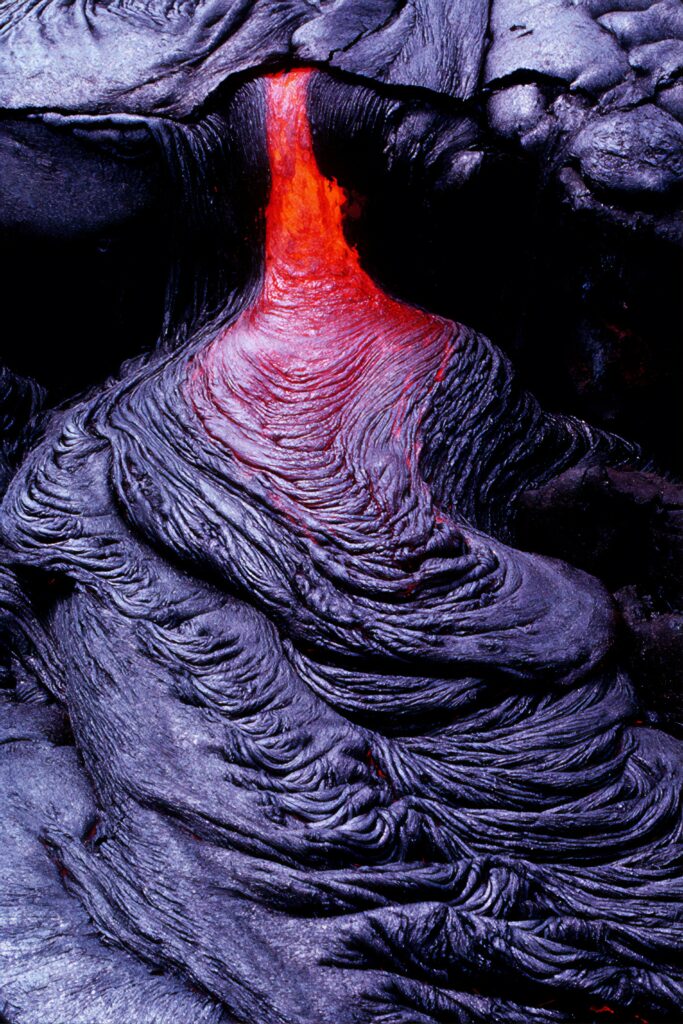 Glowing lava flowing over rugged black volcanic rock creating dramatic fiery volcanic wallpaper background