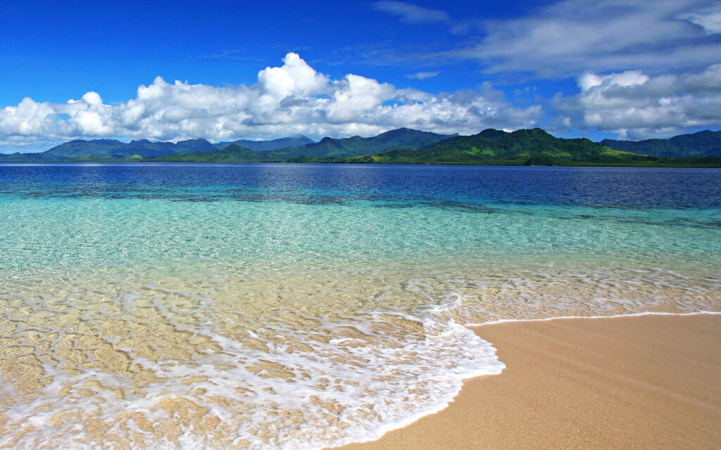 Fiji beach waves on sandy shore with turquoise water green mountains and blue sky clouds wallpaper