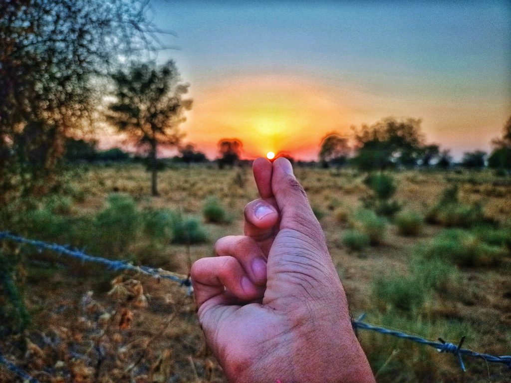 Hand making finger heart gesture at sunset over rustic field with barbed wire wallpaper background