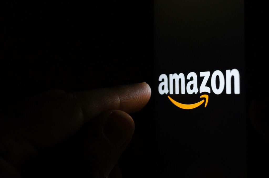 Finger poised to tap Amazon logo on dark screen highlighting online shopping technology Wallpaper