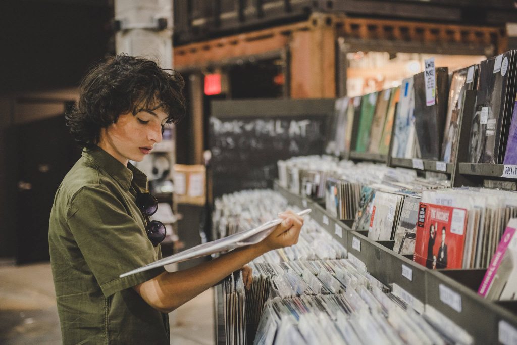Finn Wolfhard browsing vinyl records in olive shirt sunglasses warm music store indie vibe Wallpaper