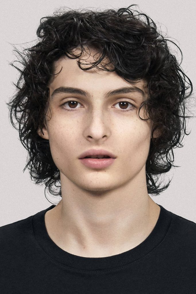 Portrait of actor Finn Wolfhard with dark curly hair in black t-shirt on grey studio background Wallpaper