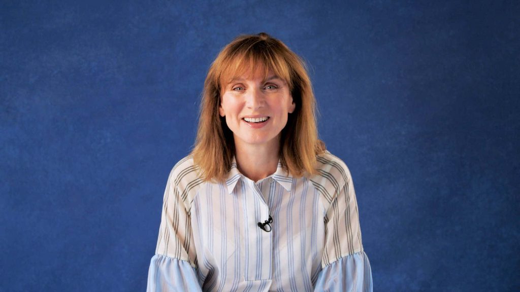 Fiona Bruce smiling in white pinstriped blouse against textured blue background professional wallpaper