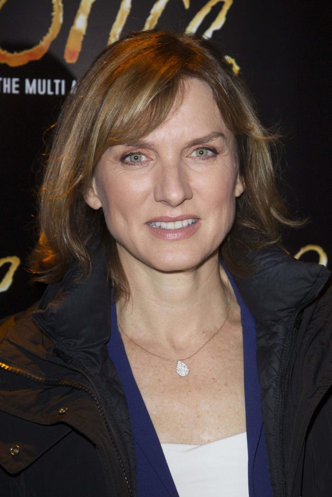 Portrait of British broadcaster Fiona Bruce smiling in dark jacket and teardrop pendant against dark backdrop Wallpaper
