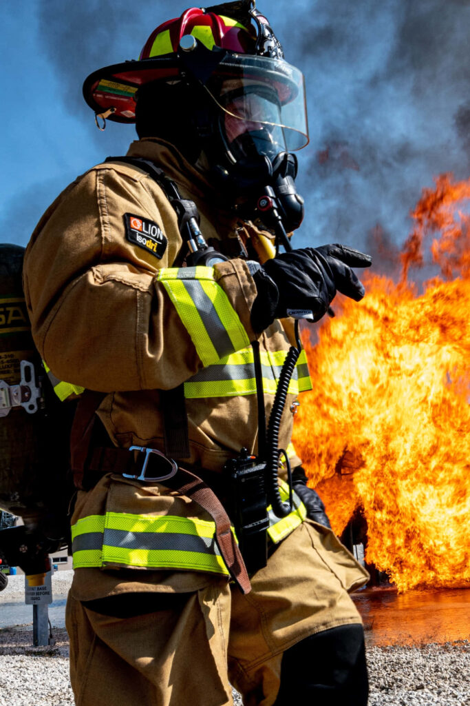 Firefighter in protective gear and gas mask standing before roaring flames ready for action Wallpaper