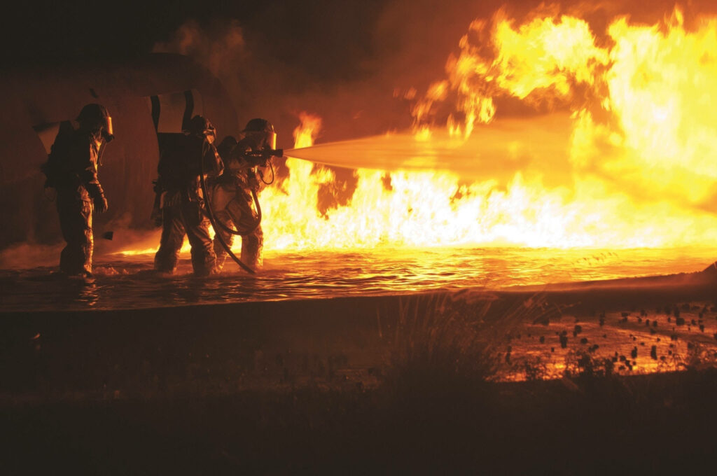 Firefighters battling massive night blaze with intense flames teamwork wallpaper background