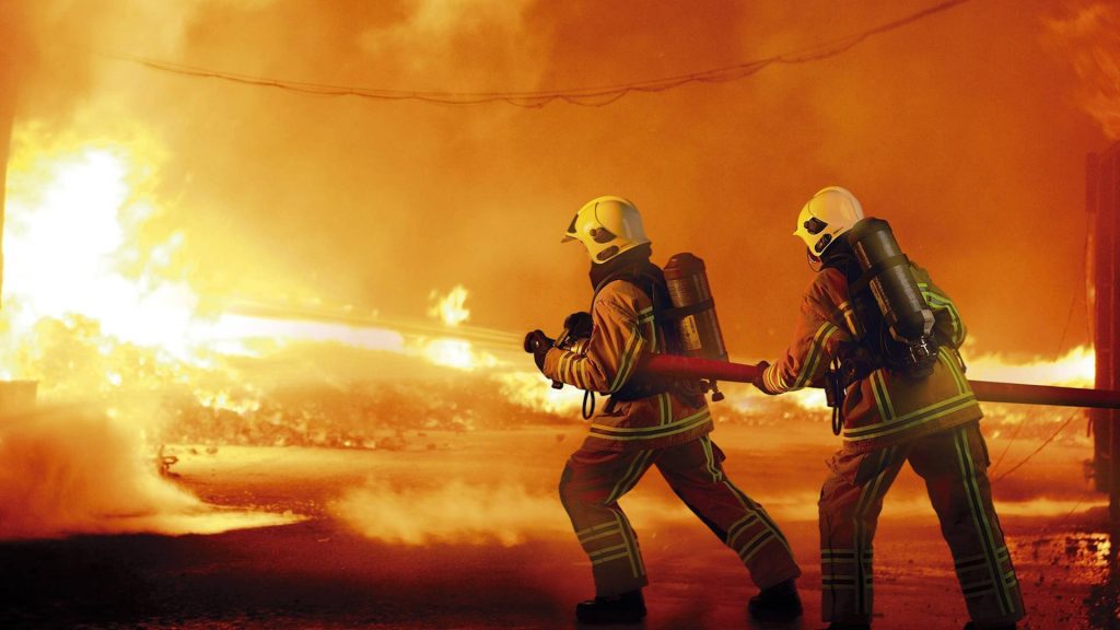 Two firefighters in full gear battling a massive fire showcasing bravery and heroism wallpaper