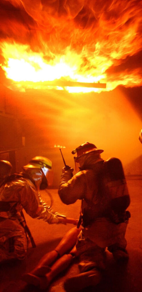 Firefighters in hazmat suits performing rescue drill amid intense flames showing teamwork and bravery Wallpaper