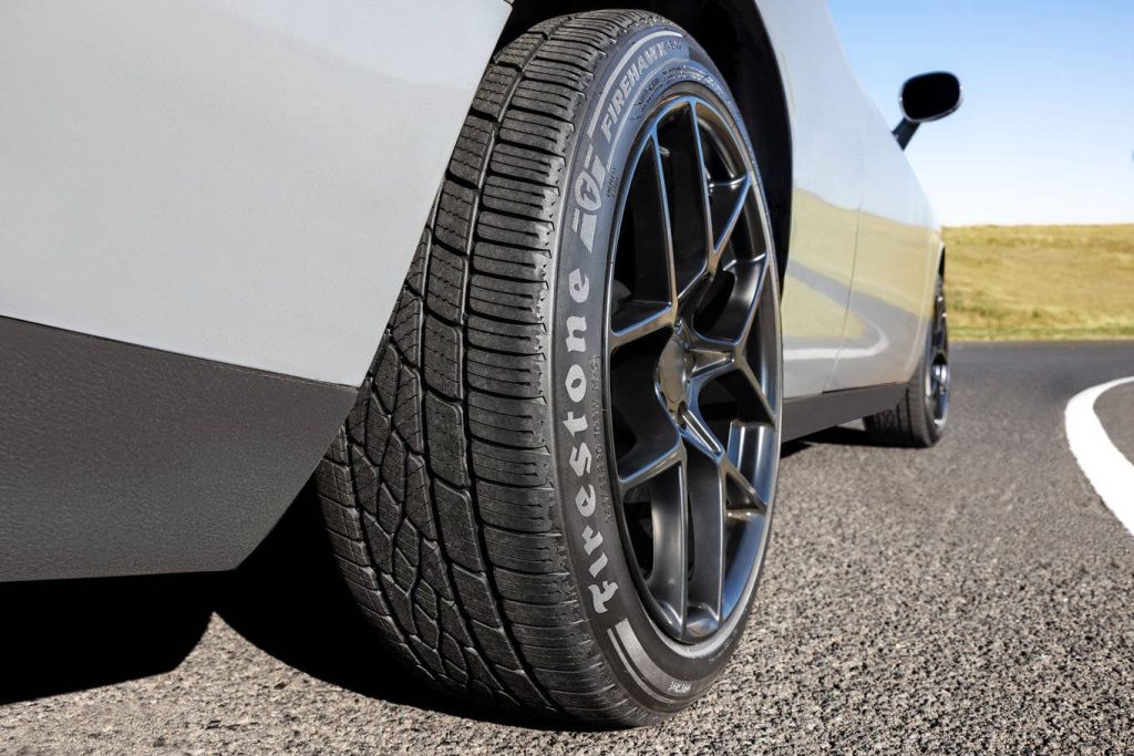 Close-up of Firestone Firehawk tire on silver sports car on sunlit asphalt road high-resolution Wallpaper