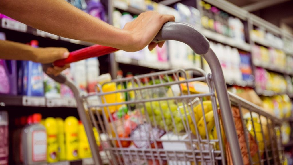 First-person view pushing shopping cart in supermarket aisle with blurred shelves background Wallpaper