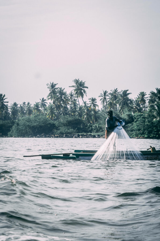 Fisherman casting net from boat in rough waves with palm trees and cloudy sky background Wallpaper