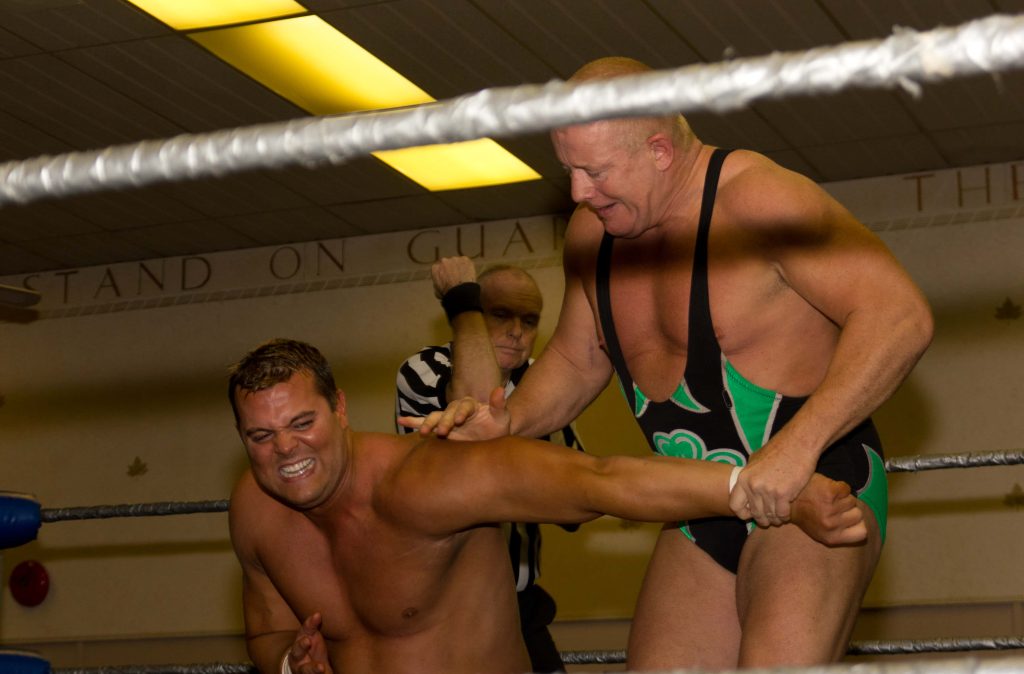 Fit Finlay grappling Harry Smith in wrestling ring with referee watching intense match action Wallpaper
