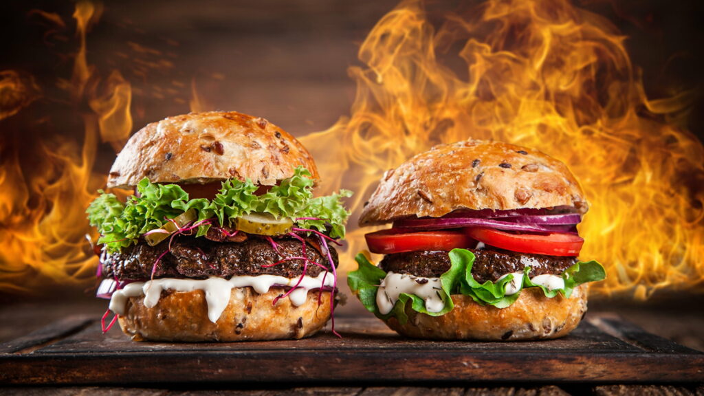 High-resolution wallpaper of two gourmet hamburgers with fresh toppings on wooden board flames background