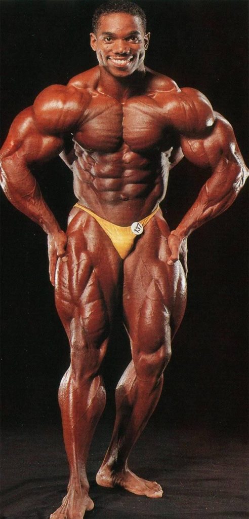 Flex Wheeler posing in yellow trunks showing shredded muscular physique on black backdrop wallpaper