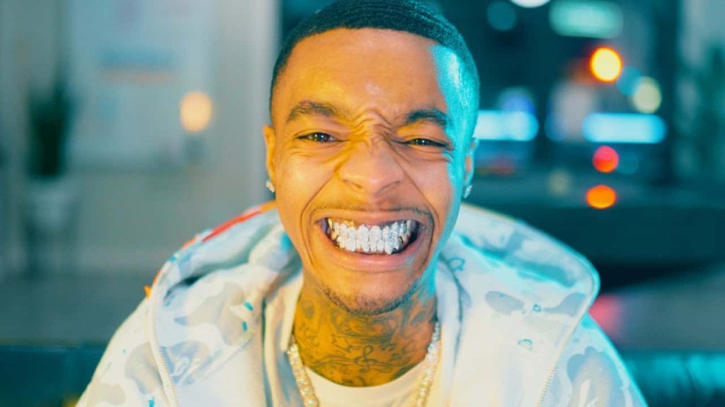 HD wallpaper of FlightReacts smiling with diamond grills in patterned hoodie vibrant studio background