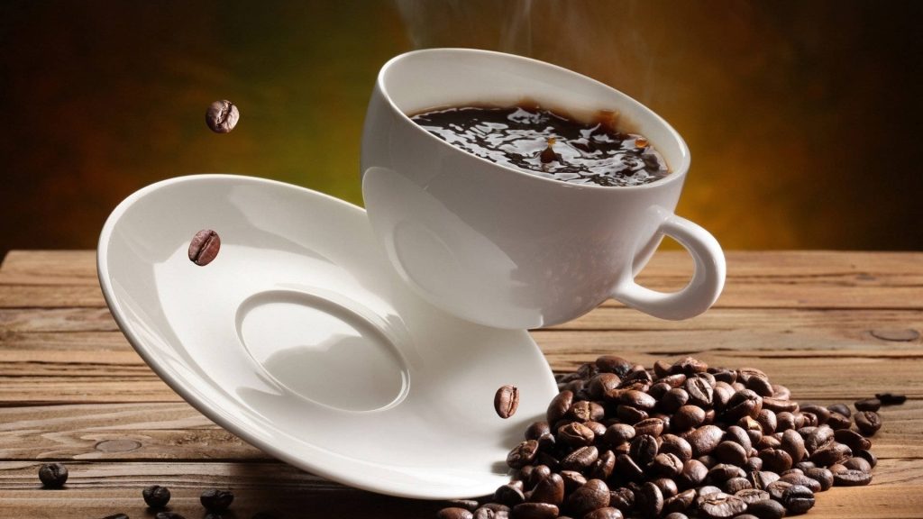 White coffee cup and saucer floating above roasted coffee beans on rustic wooden table background Wallpaper
