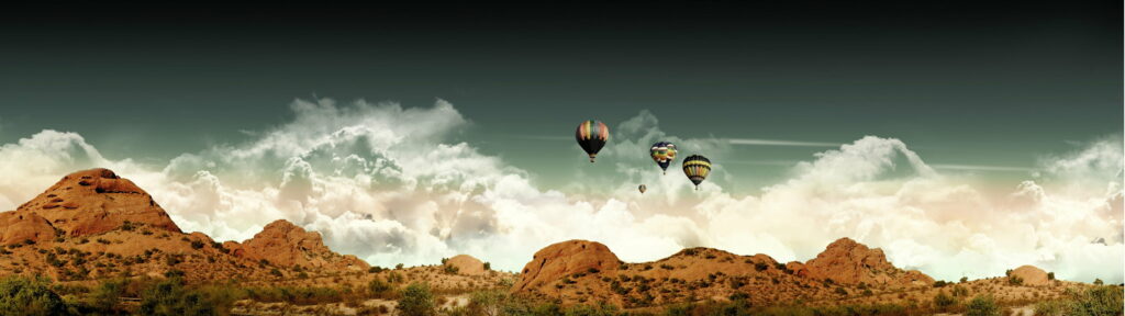 Colorful hot air balloons float over red rock desert under cloudy sky panoramic wallpaper background