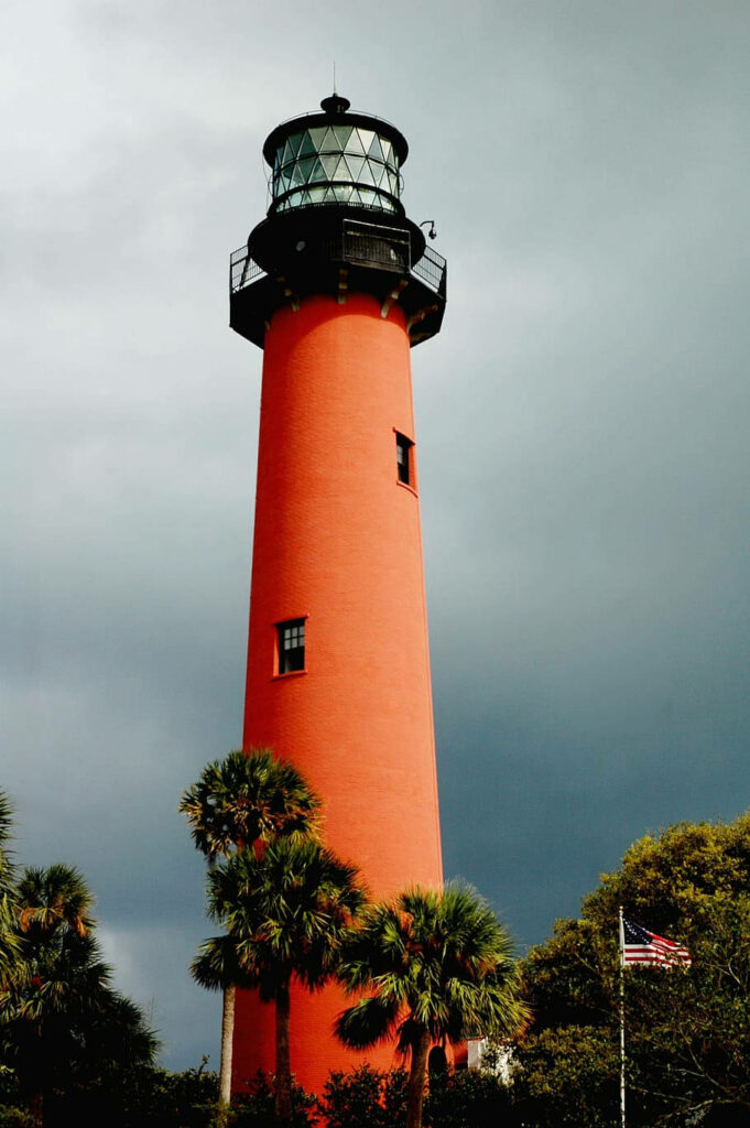 Red Florida lighthouse with palm trees under dramatic cloudy sky coastal wallpaper background
