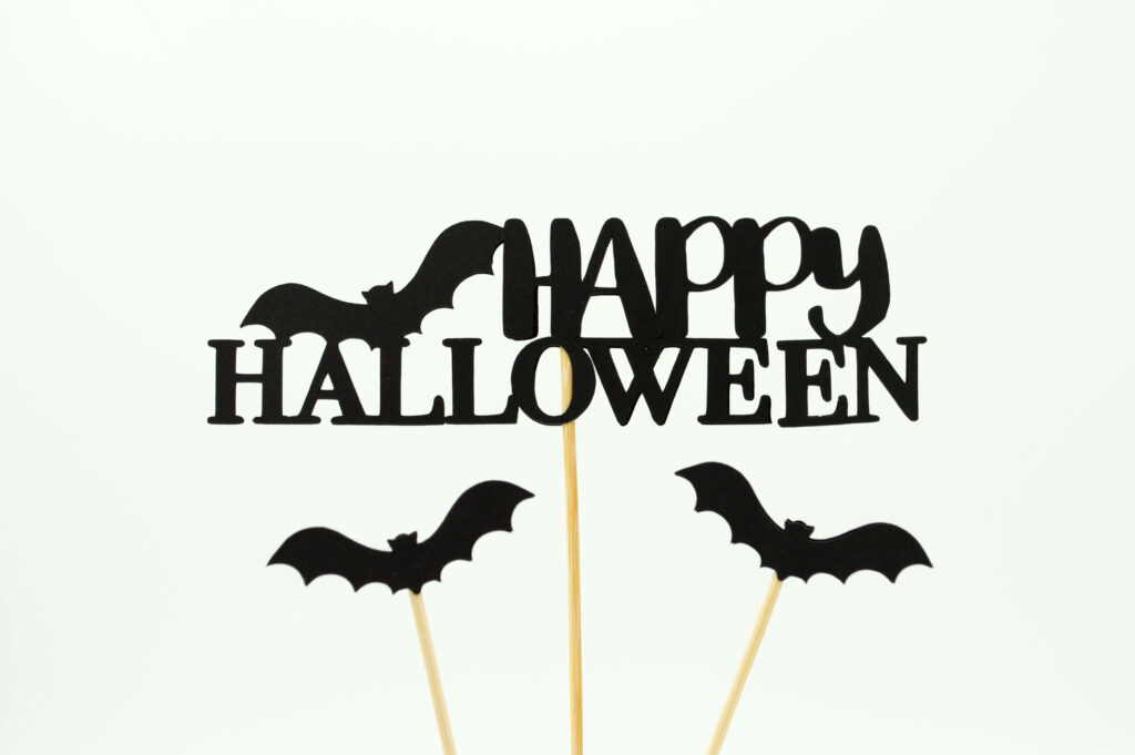 Minimalist Happy Halloween cake topper with black bats on skewers on white background wallpaper