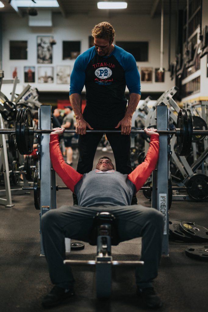 Focused athlete bench pressing with trainer in professional gym inspiring strength and dedication Wallpaper