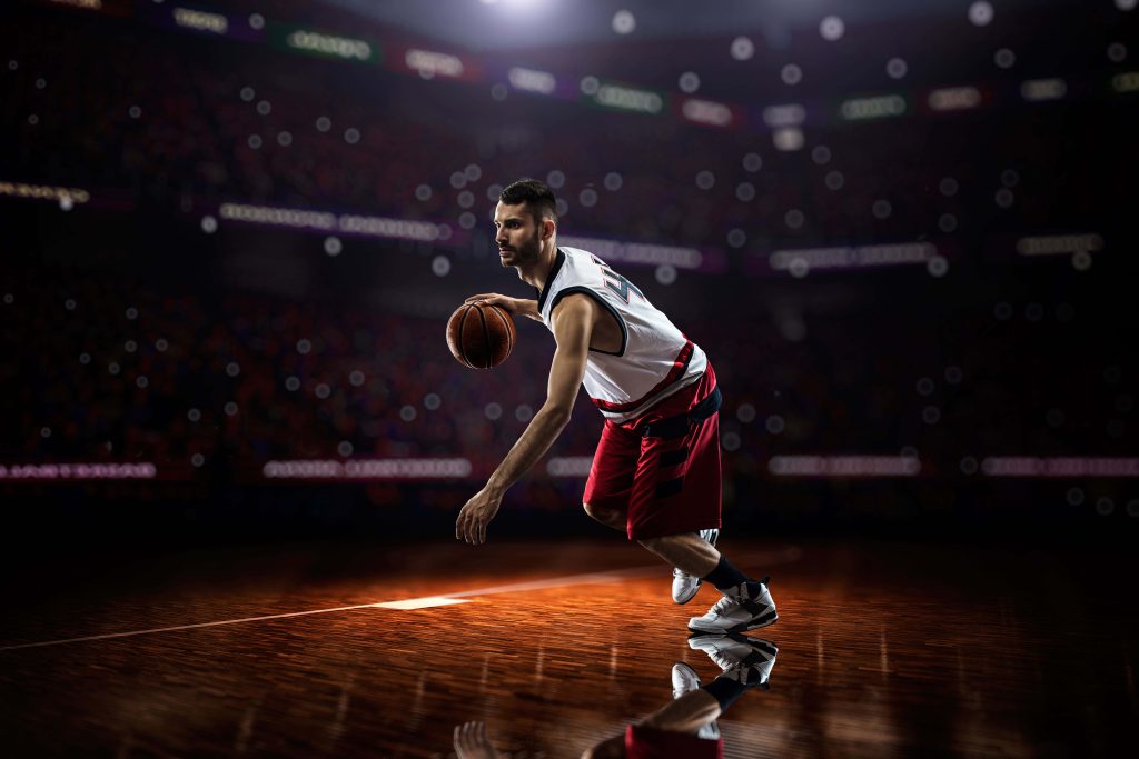 Focused basketball player dribbling on reflective court in dramatic lit dark stadium background wallpaper