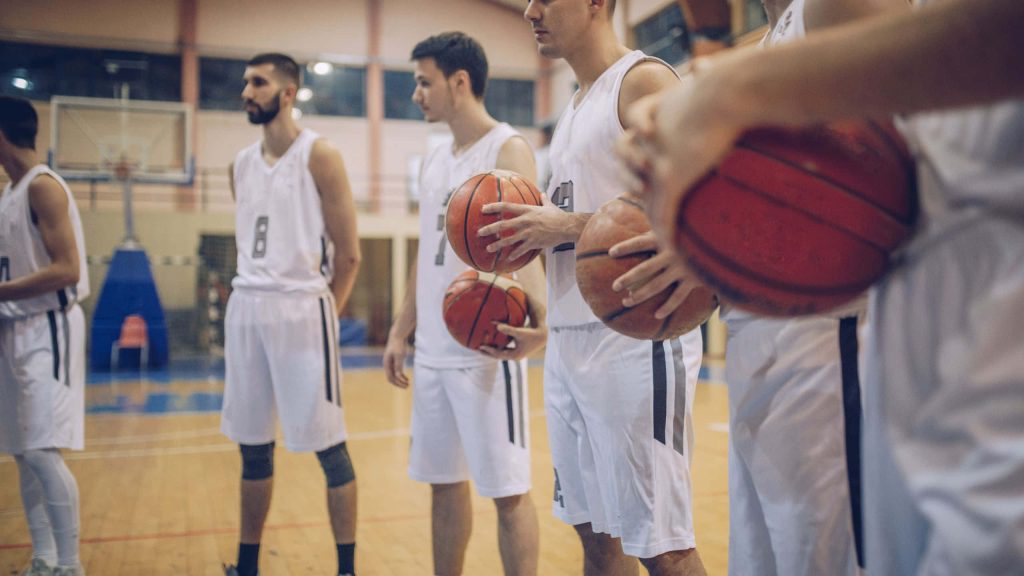 Basketball team in white uniforms practicing indoors on polished wooden court holding basketballs Wallpaper