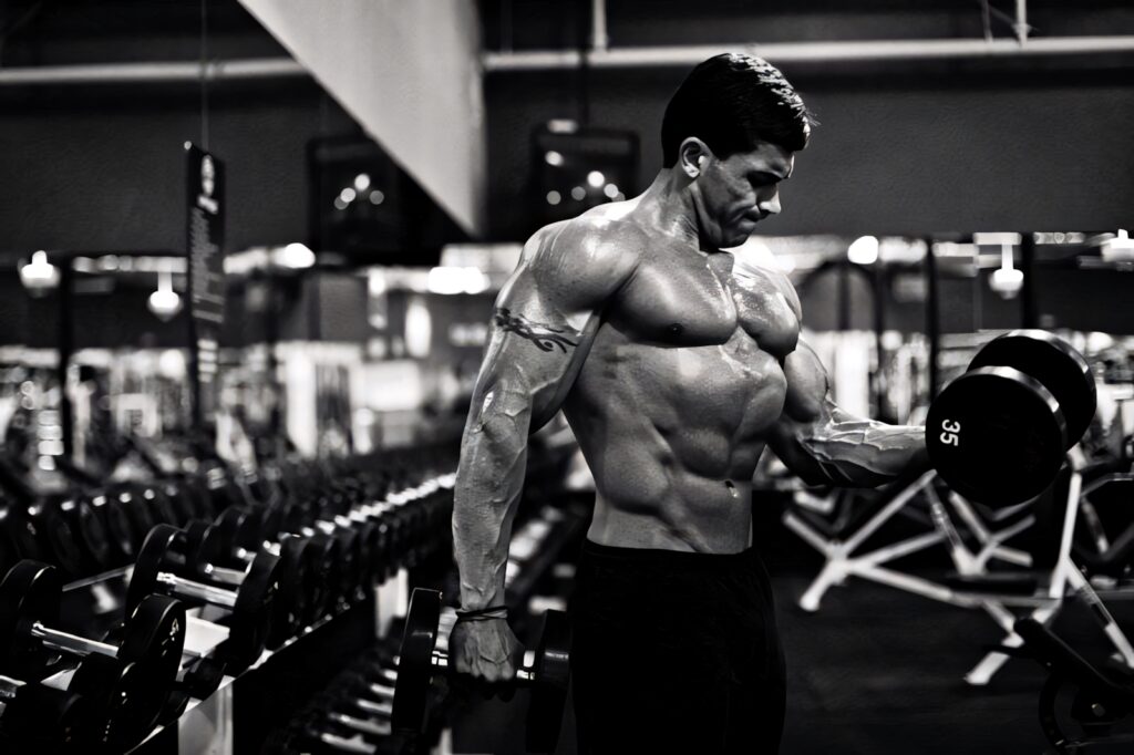 Focused bodybuilder lifting dumbbells in gym showcasing muscular strength and definition wallpaper