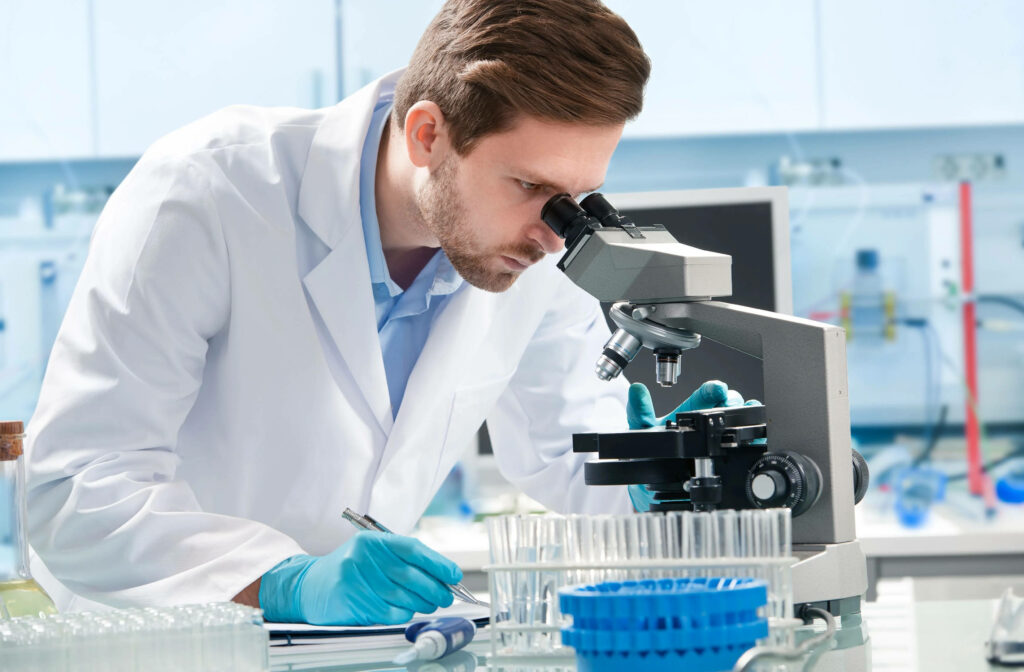 Doctor in white lab coat examining samples through microscope in modern medical research lab Wallpaper