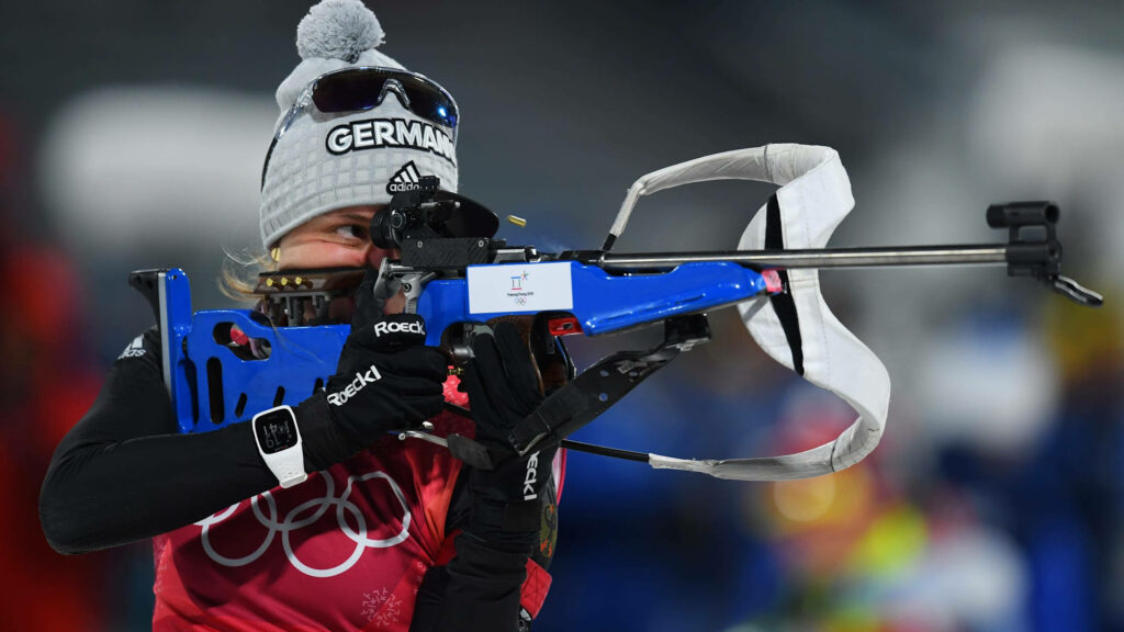 Focused Female Biathlete Aiming in Winter Sports Wallpaper