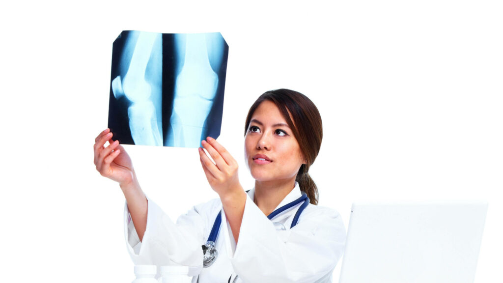 Female doctor in white coat examining knee joint X-ray in modern medical setting bright background Wallpaper