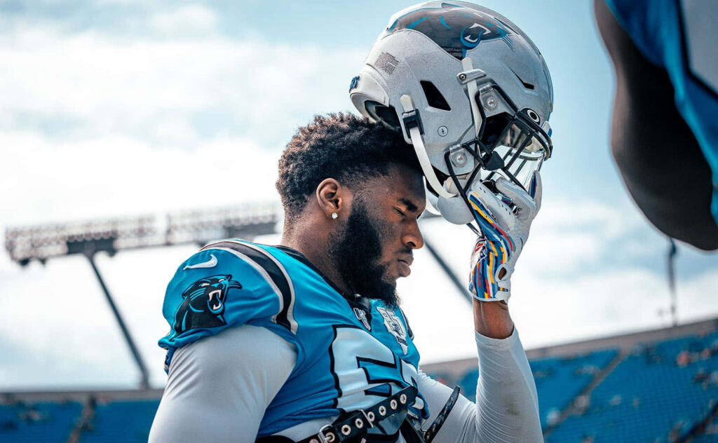 Brian Burns focused holding helmet in Carolina Panthers uniform at sunlit stadium pre-game moment Wallpaper