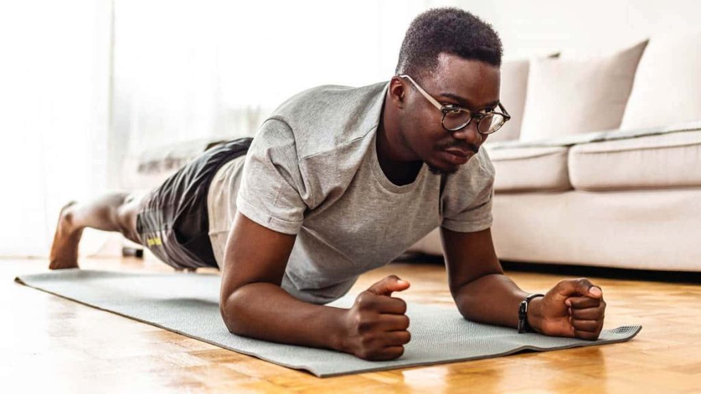 Man with glasses doing plank exercise on yoga mat in bright modern living room workout Wallpaper