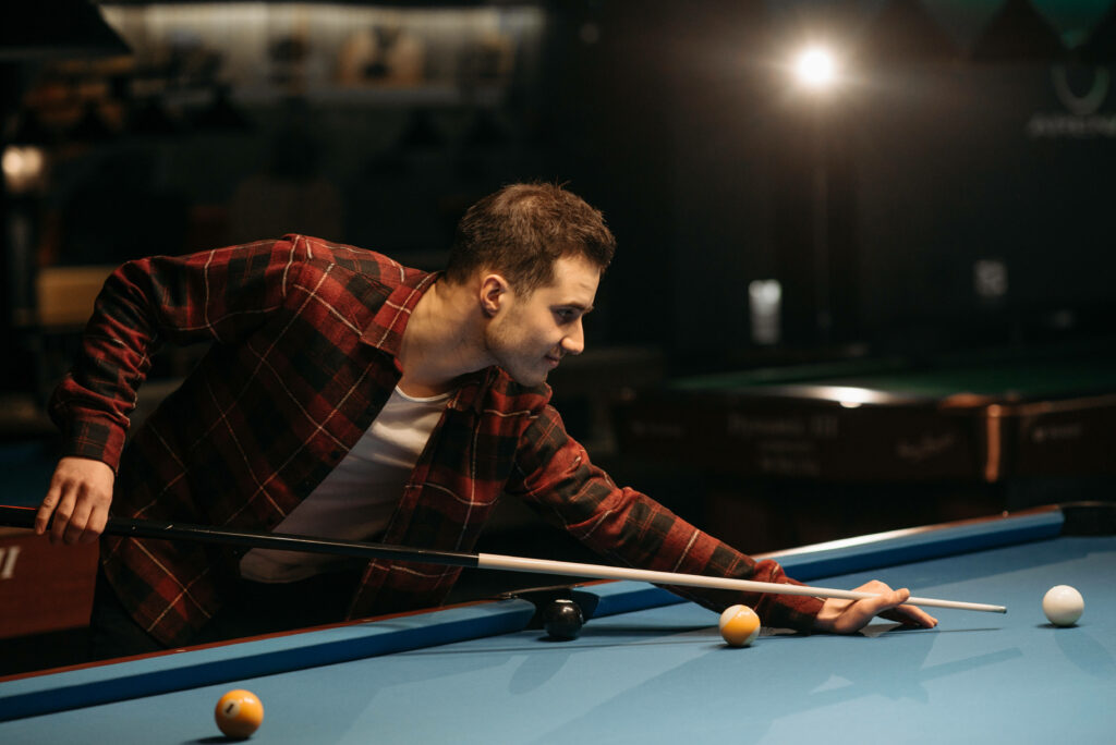 Man aiming a precise billiards shot in a dimly lit pool hall showing skill and focus Wallpaper
