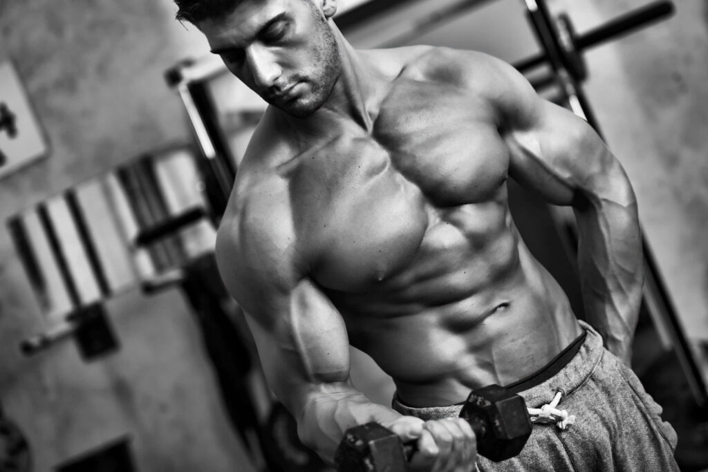 Muscular man lifting dumbbell in gym showing strength dedication and defined physique wallpaper