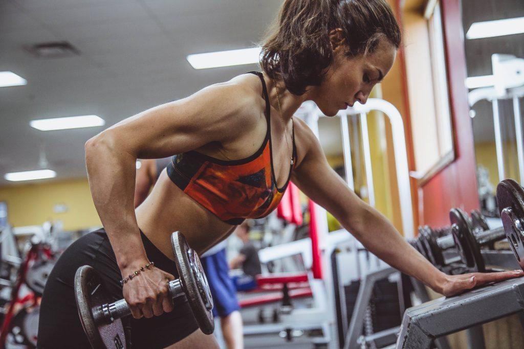Fit woman in orange sports bra doing single-arm dumbbell row showcasing muscle strength Wallpaper