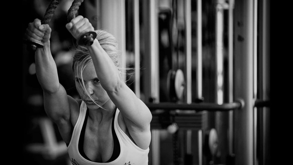 Focused woman doing cable rope exercise in gym black and white fitness wallpaper motivation background