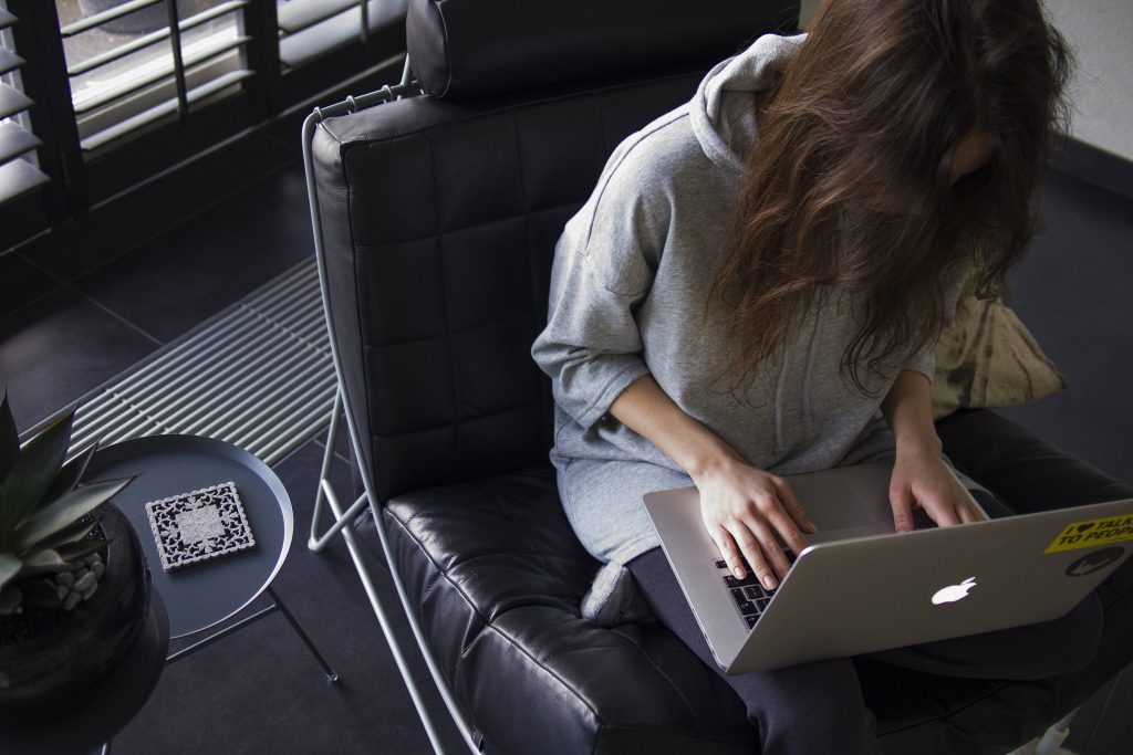 Woman in gray hoodie focused editing on MacBook in minimalist workspace with succulent plant Wallpaper