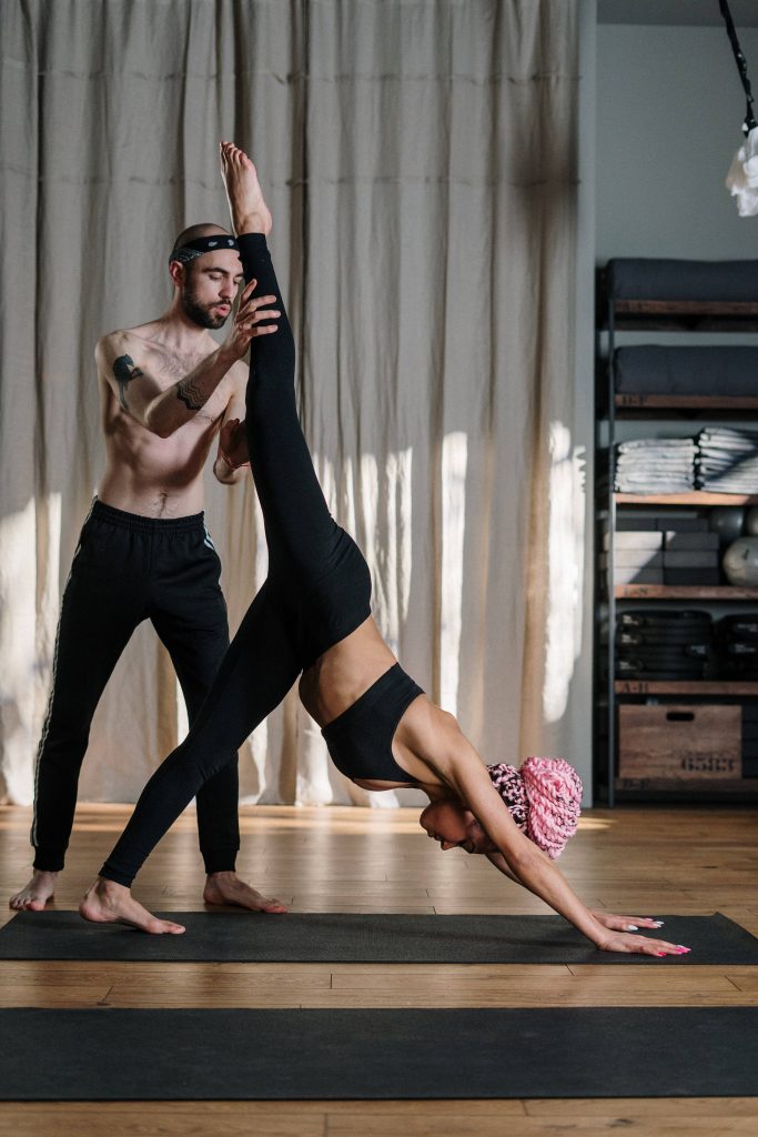 Male yoga instructor guides woman in one-legged downward dog pose in sunlit studio fitness training Wallpaper