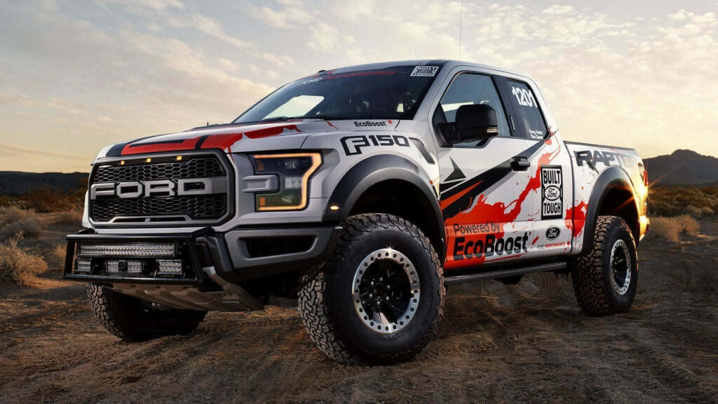 Ford F-150 Raptor driving on rugged dirt road showcasing bold design and off-road power background Wallpaper
