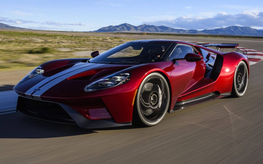 Glossy red Ford GT racing stripes speeding on track with motion blur and mountain backdrop wallpaper